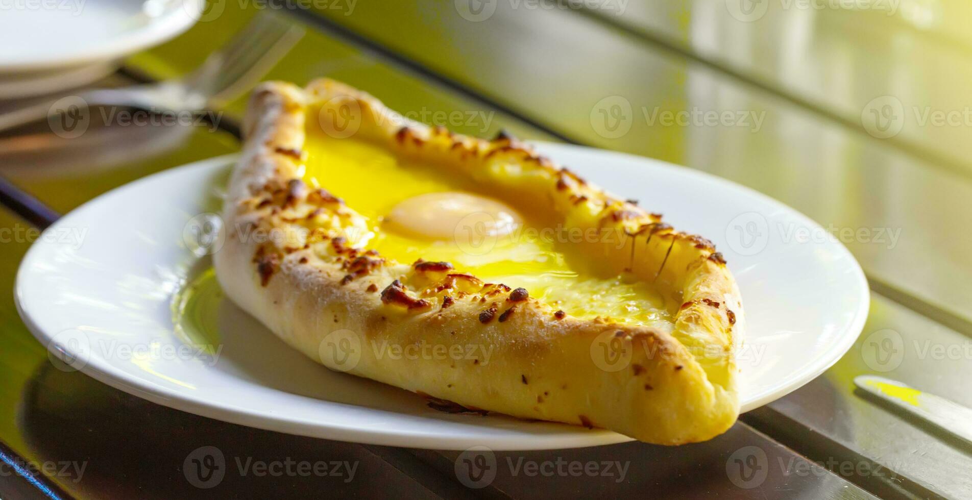 Adjara-style khachapuri, baked dough with egg, cheese and two pieces of butter on a white plate in a cafe. photo