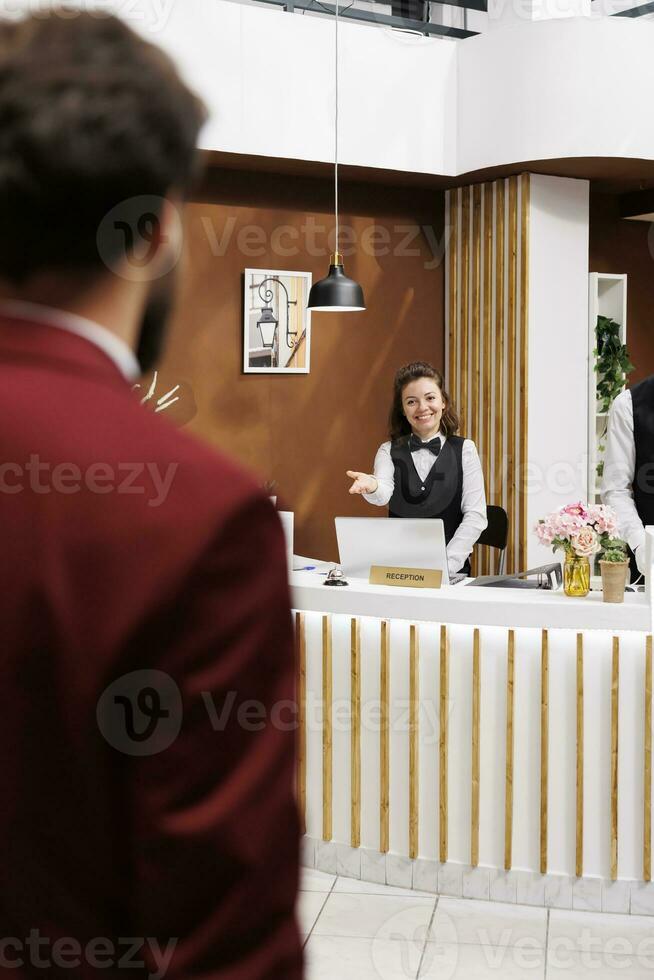 Employee welcoming businessman in lobby, providing luxury services for guest travelling on work trip. Guest arriving at resort with baggage, receiving friendly assistance from hotel staff. photo