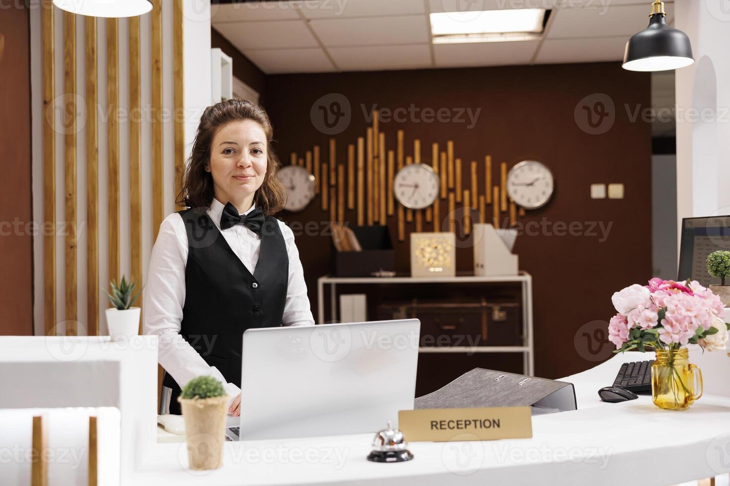 Friendly receptionist at front desk prepared to greet guests in hotel lobby, providing excellent customer services to ensure pleasant stay. Concierge working at reception, welcome people. photo