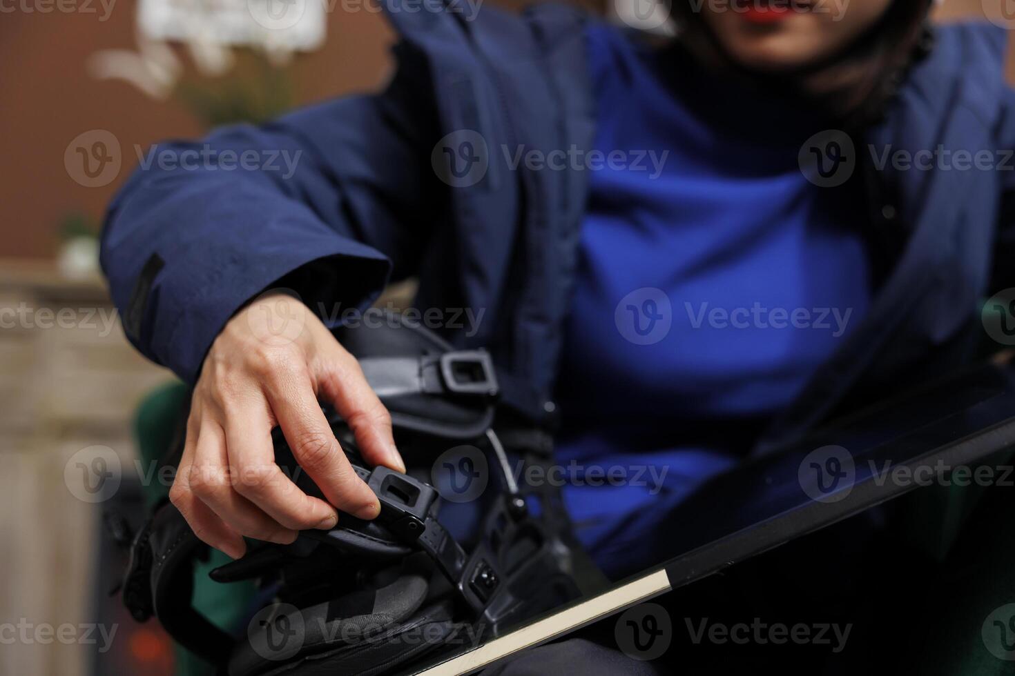 Close up shot of tourist securing snowboarding gear in hotel foyer, prepared for winter vacation at ski resort. Detailed view of person inspecting a snowboard, getting ready for snowy adventure. photo
