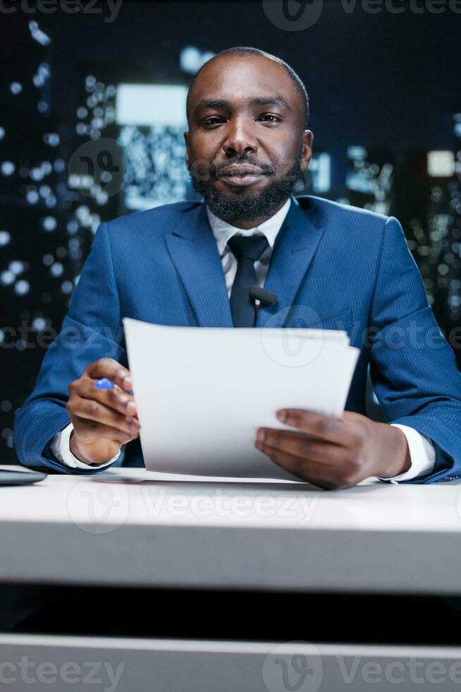 TV host reporting daily events news in studio, going live on midnight broadcast to discuss important incidents worldwide. African american journalist presenting information and details. photo