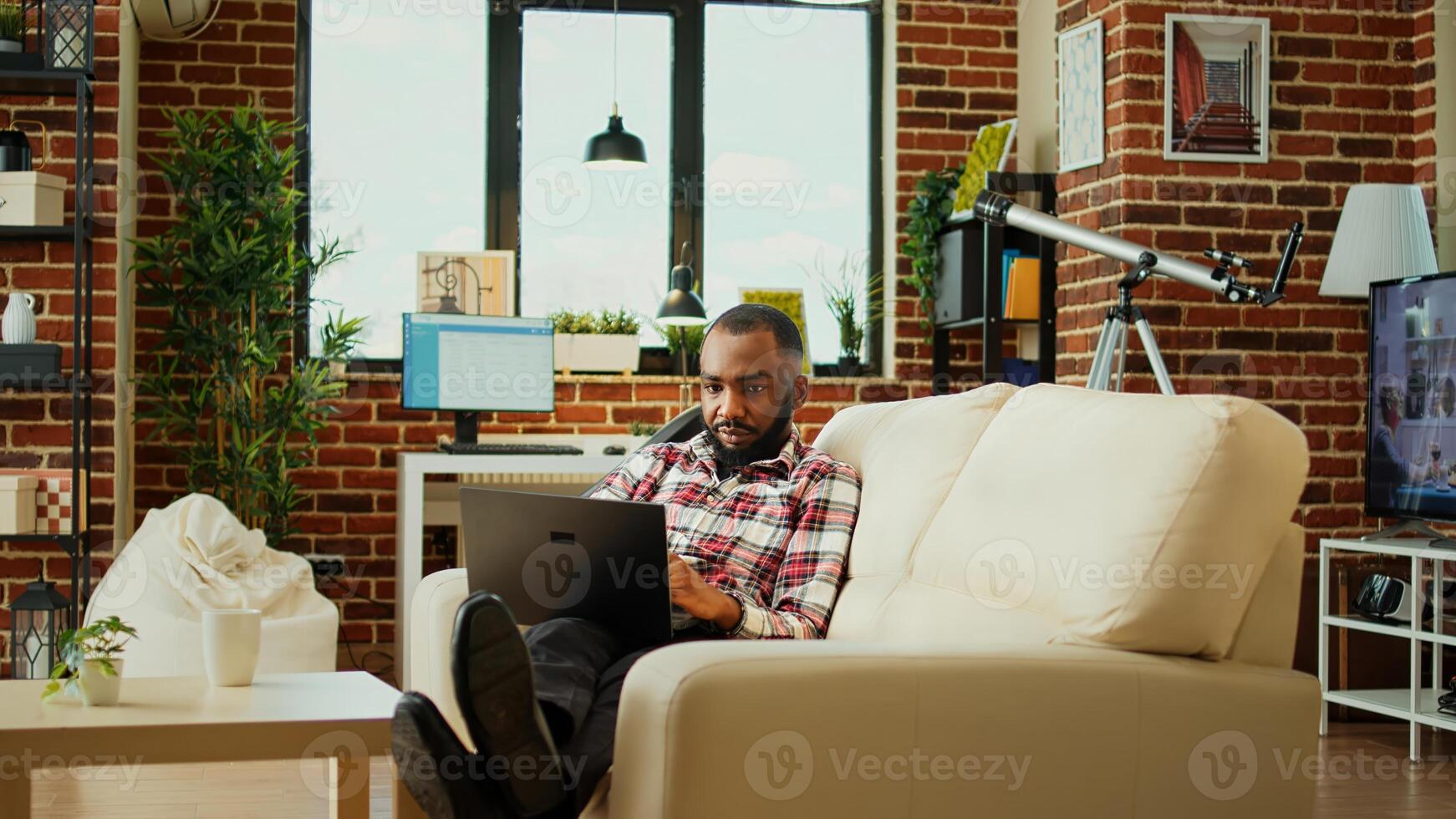 Relaxed freelancer inputing data on laptop while working from home. African american teleworker lying on couch, remotely performing tasks in nice stylish warm apartment living room photo