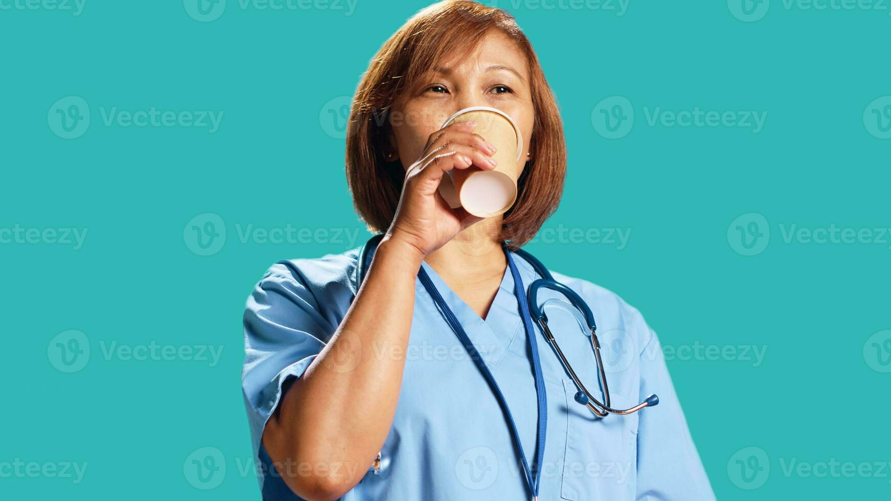 Satisfied BIPOC healthcare expert enjoying fresh cup of coffee during job shift break. Happy certified nurse isolated over studio background drinking hot beverage, close up photo