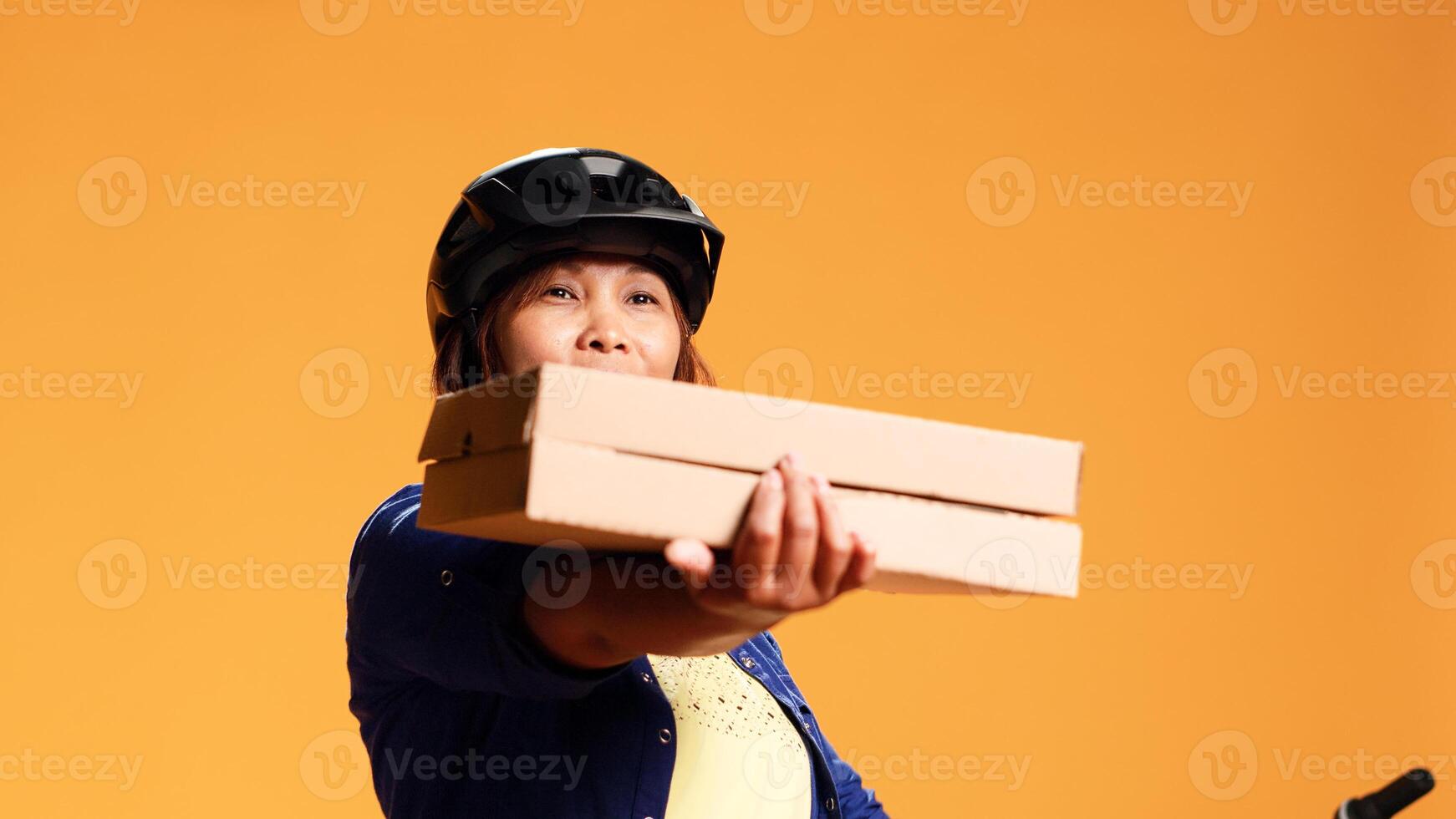 cadera nivel cerca arriba Disparo de alegre mensajero mirando a cámara, demostración aprobación gesto mientras entregando eliminar comidas. simpático ciclista ofrecimiento Pizza a cliente, aislado terminado estudio antecedentes foto