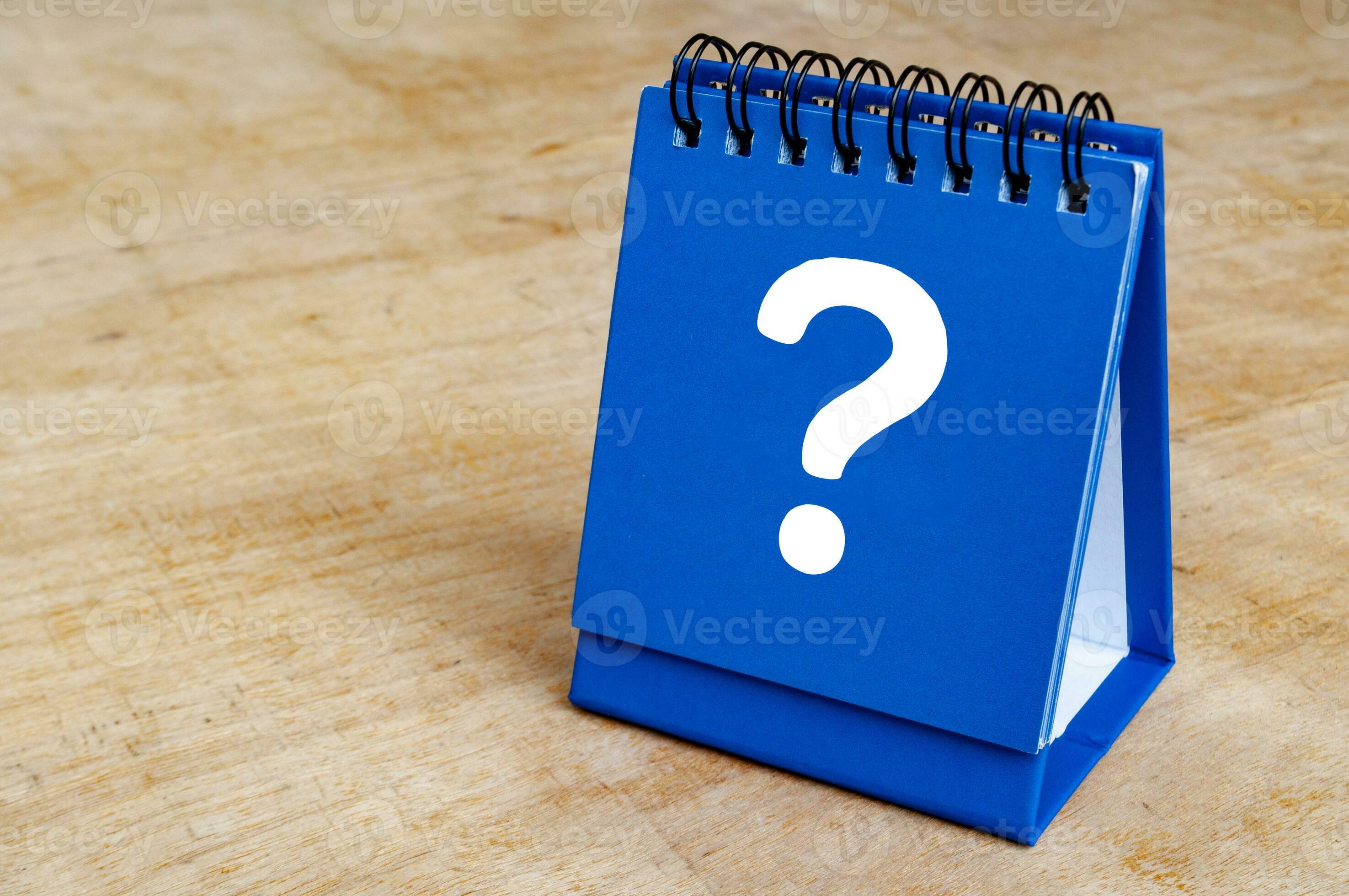 Question mark on blue notepad on wooden background. Question and answer