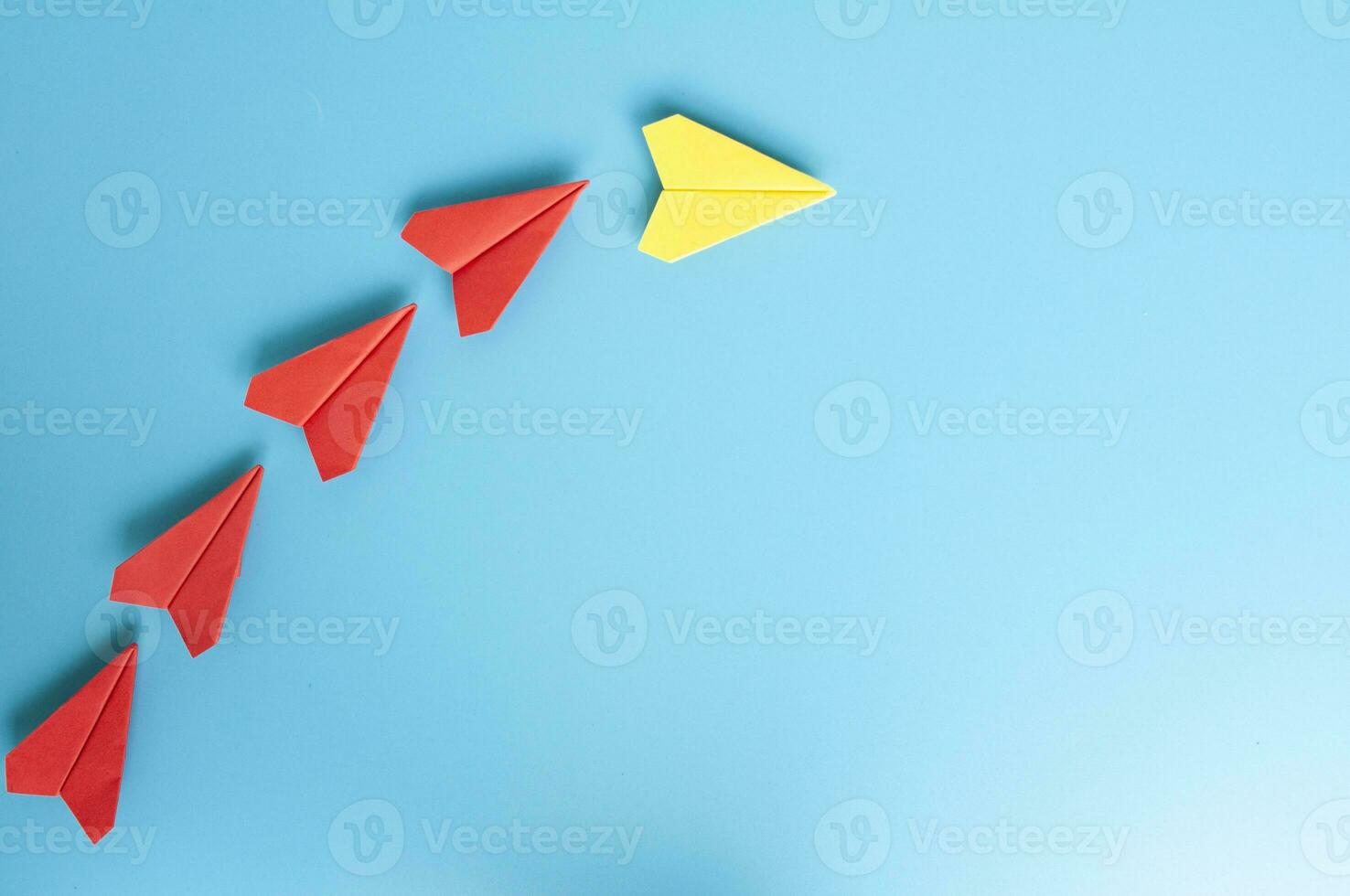 Top view of yellow paper airplane origami leading red paper airplanes on blue cover background photo