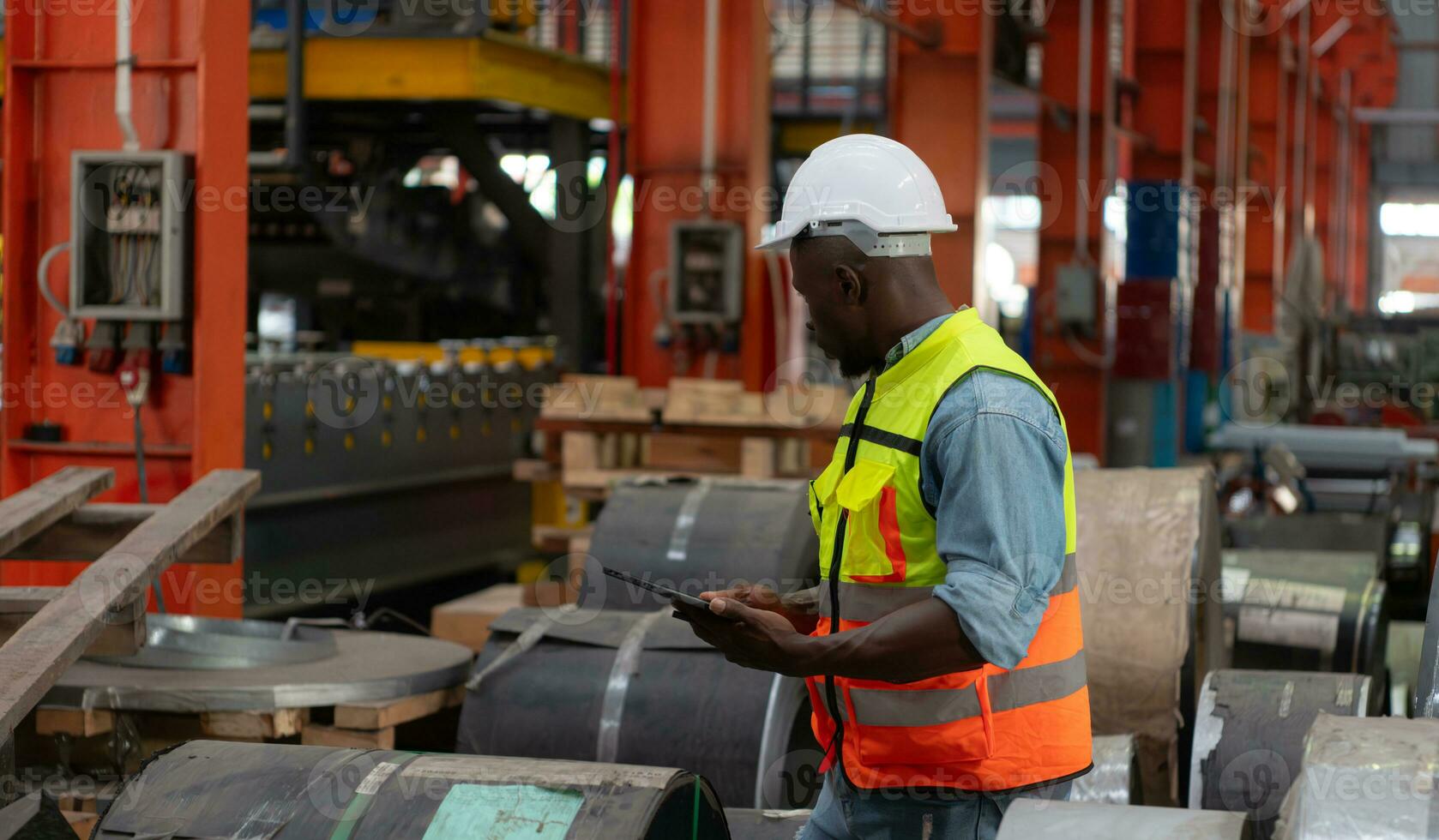 Front view of young man worker using digital tablet to check stock in metal sheets storage of factory photo