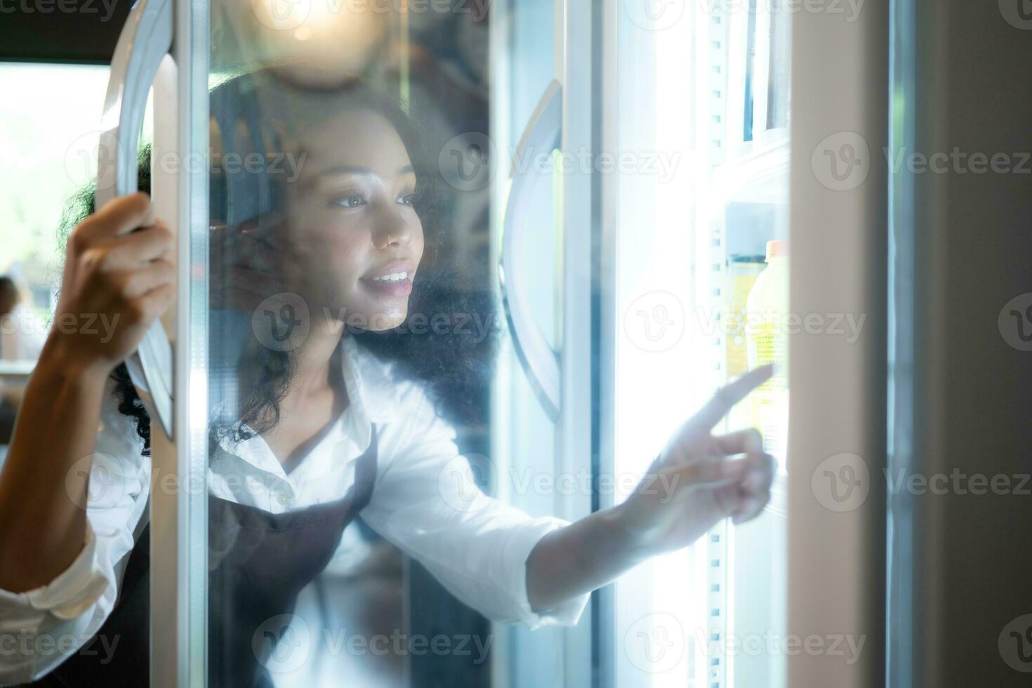 The owner of a coffee shop looks inside the refrigerator to retrieve chilled food to serve a customer. photo
