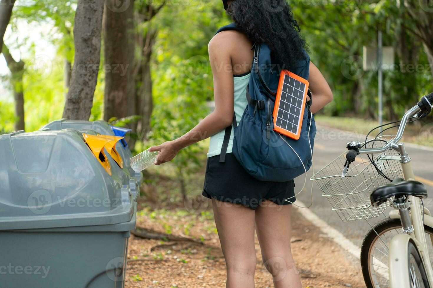 Rear view of a young woman collecting garbage in the park. It has a backpack with a solar panel for charging smartphone. photo