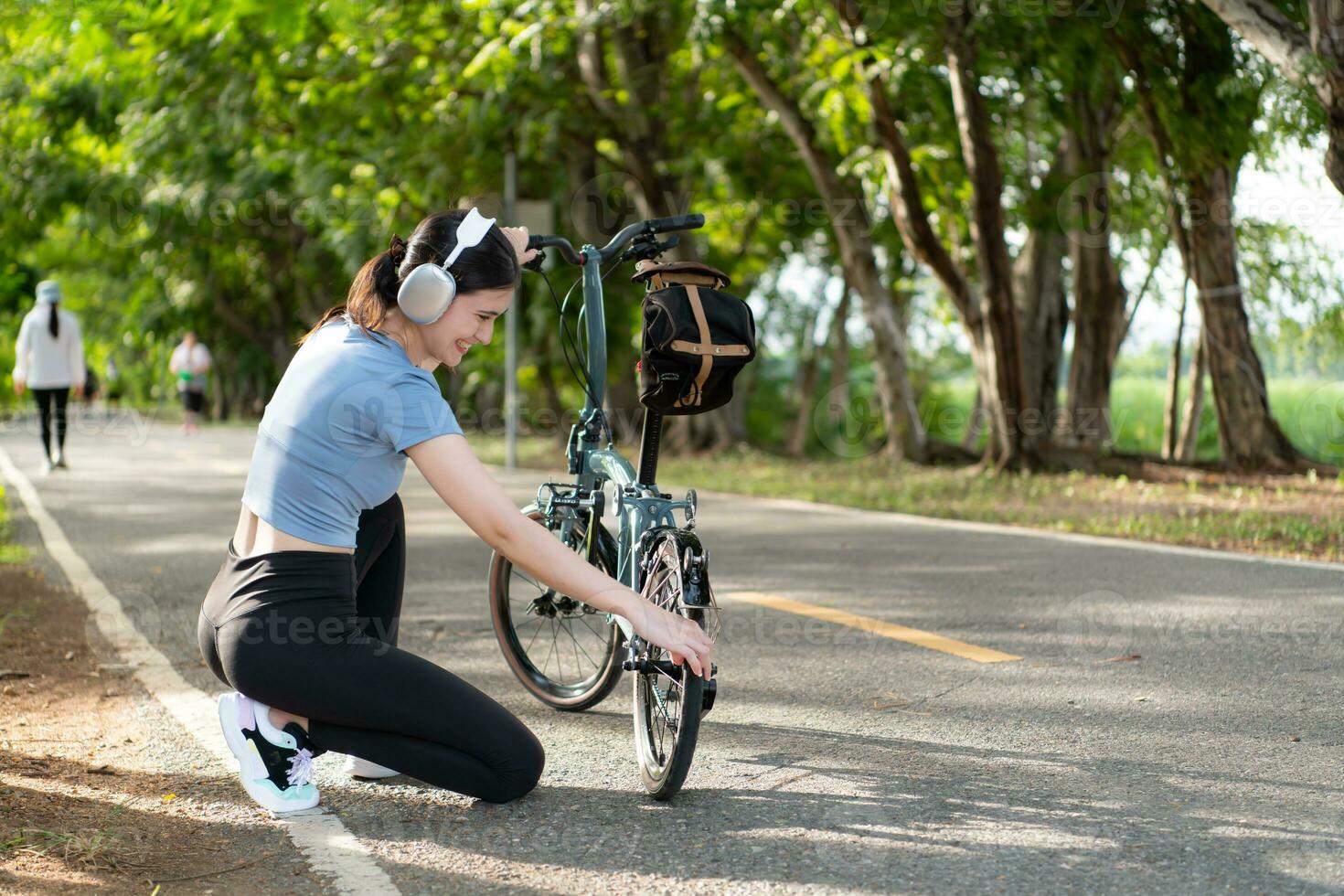 A young woman listens to music with headphones while checking the readiness of her bicycle. before driving on a bike path in the park photo