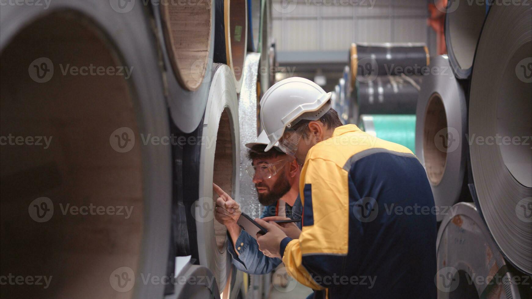 A team of young men working in a warehouse storing rolls of metal sheets. Inspecting the metal sheet rolls stored in the warehouse to be imported onto the metal sheet production line. photo