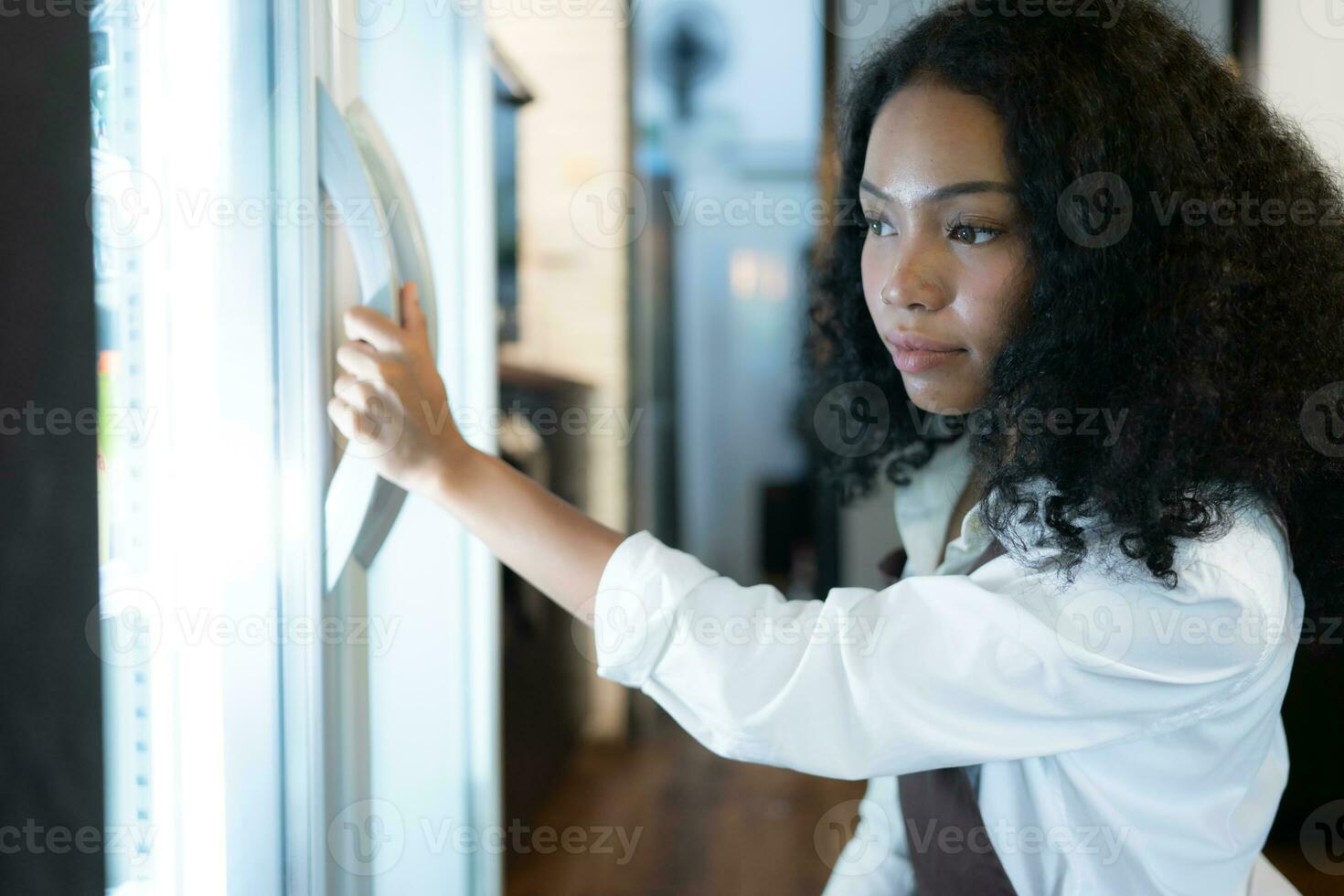 The owner of a coffee shop looks inside the refrigerator to retrieve chilled food to serve a customer. photo