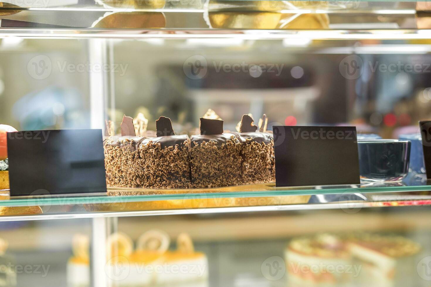 Closeup of chocolate cake behind glass of showcase in pastry shop photo