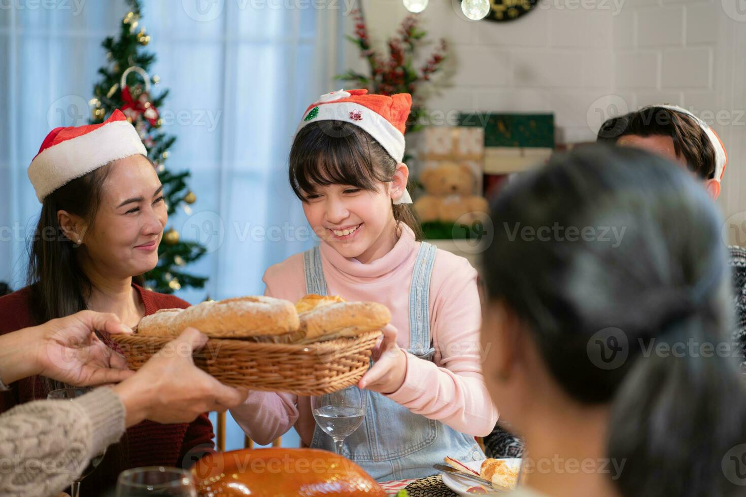 Happy family celebrating Christmas together at home. Cheerful parents and children in Santa hat giving basket with bread to their children. photo