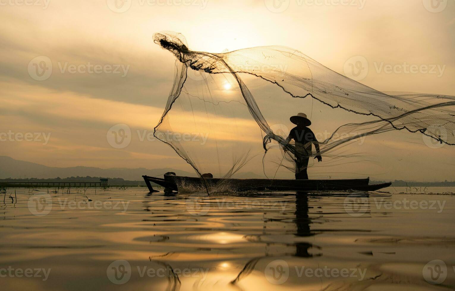 Silhouette of fisherman at sunrise, Standing aboard a rowing boat and casting a net to catch fish for food photo