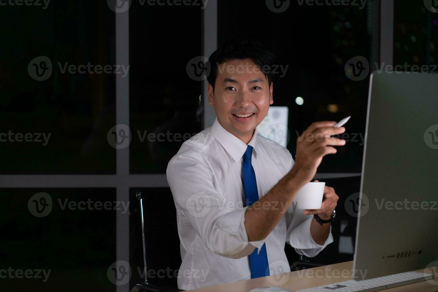 Young Asian broker international stock traders working at night in office using computer and drink coffee. photo