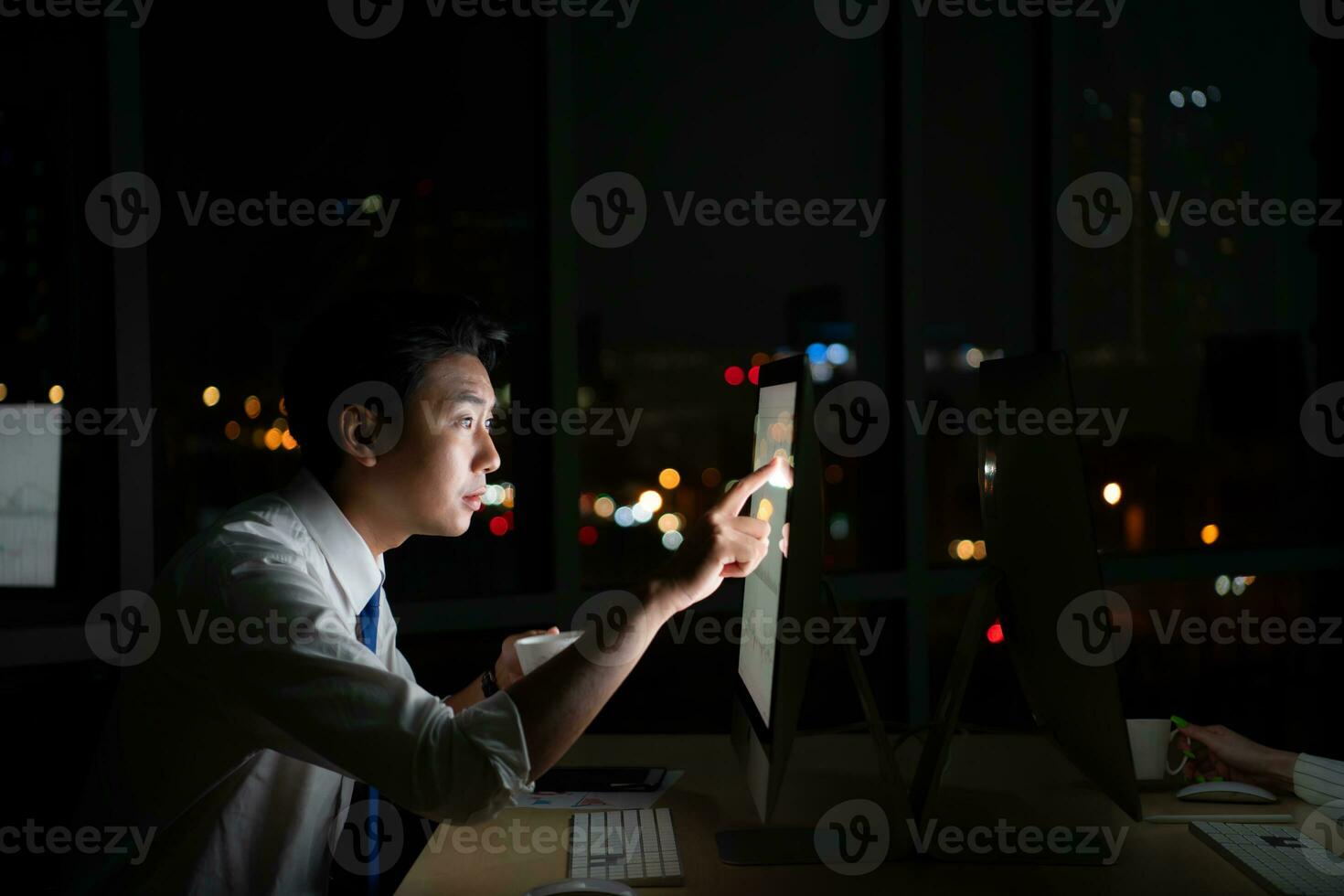 Young Asian broker international stock traders working at night in office using computer and thinking. photo