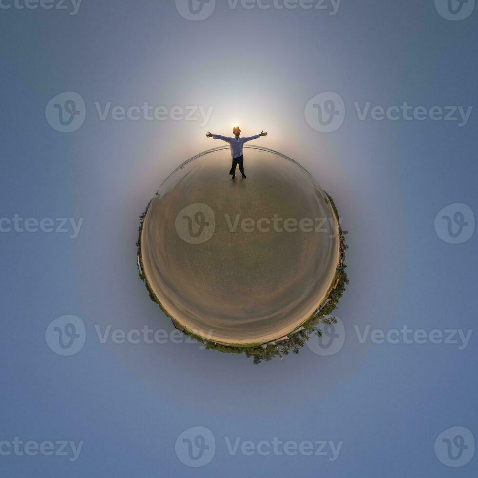 tiny planet in blue sky with happy man joyfully stands on seashore in rays of evening tropical sun with transformation of spherical panorama 360 degrees. Curvature of space. photo
