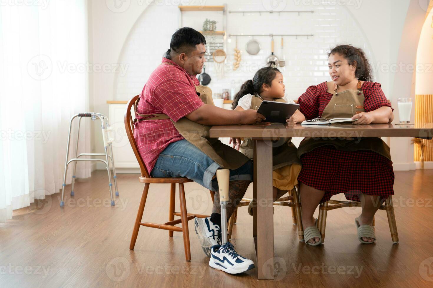 un talla extra familia con un padre vistiendo un protésico pierna, es felizmente ayudando un niño con su deberes y teniendo divertido juntos en el comida habitación de el casa antes de Cocinando juntos foto