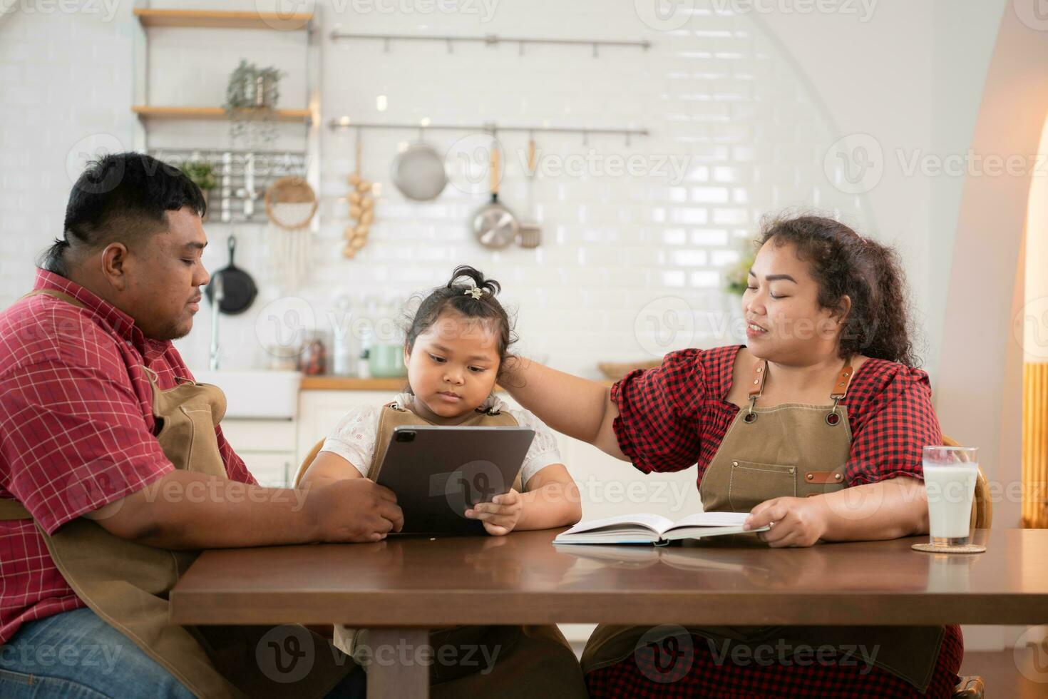 A plus-size family with a father wearing a prosthetic leg, is happily assisting a child with her homework and having fun together in the dining room of the house before cooking together photo