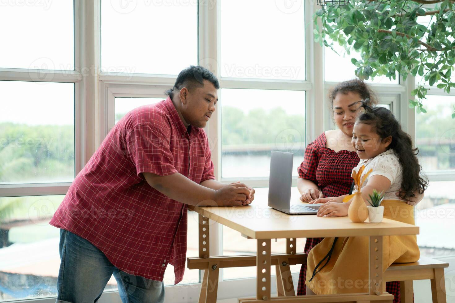 A plus-size family with a father wearing a prosthetic leg, is happily assisting a child with her homework and having fun together in the balcony of the house photo