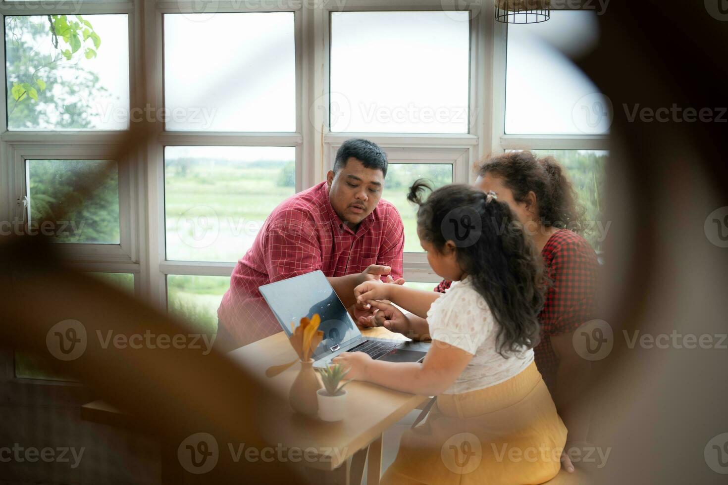 A plus-size family with a father wearing a prosthetic leg, is happily assisting a child with her homework and having fun together in the balcony of the house photo