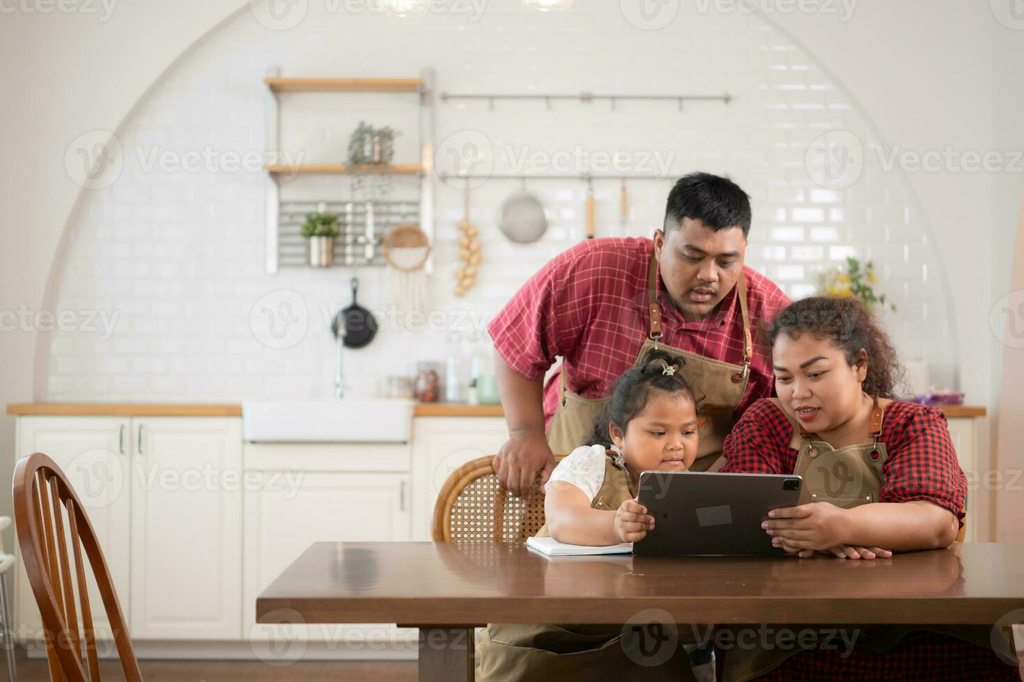A plus-size family with a father wearing a prosthetic leg, is happily assisting a child with her homework and having fun together in the dining room of the house before cooking together photo