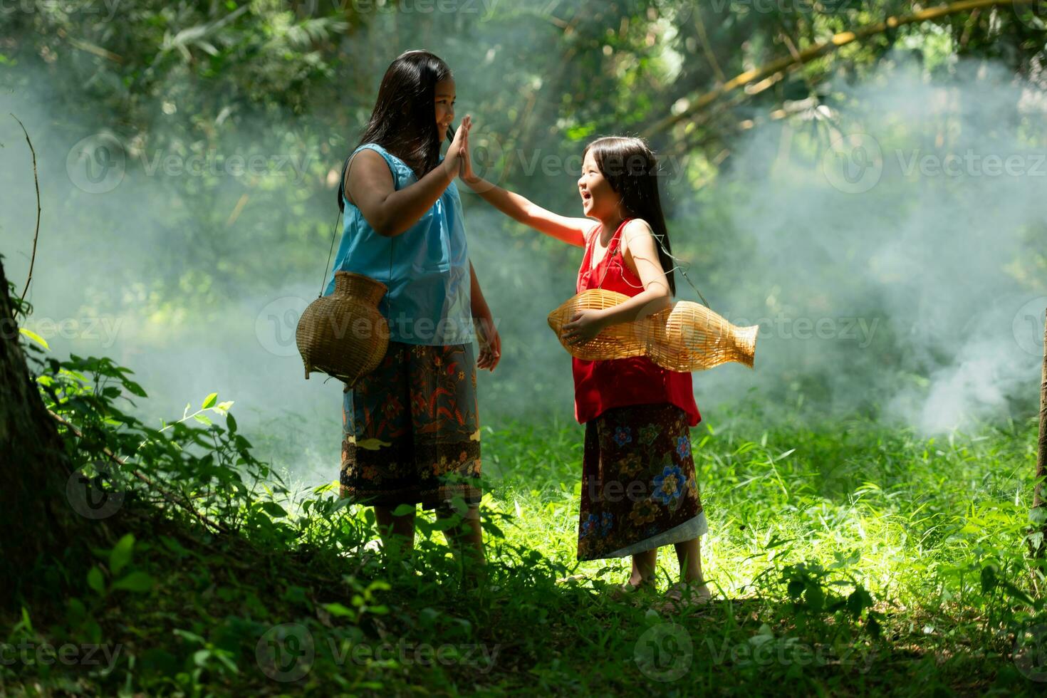 Two girls Asian women with traditional clothing stand in the rainforest. They had fun playing together before assisting Grandpa in catching fish in a nearby lake. photo