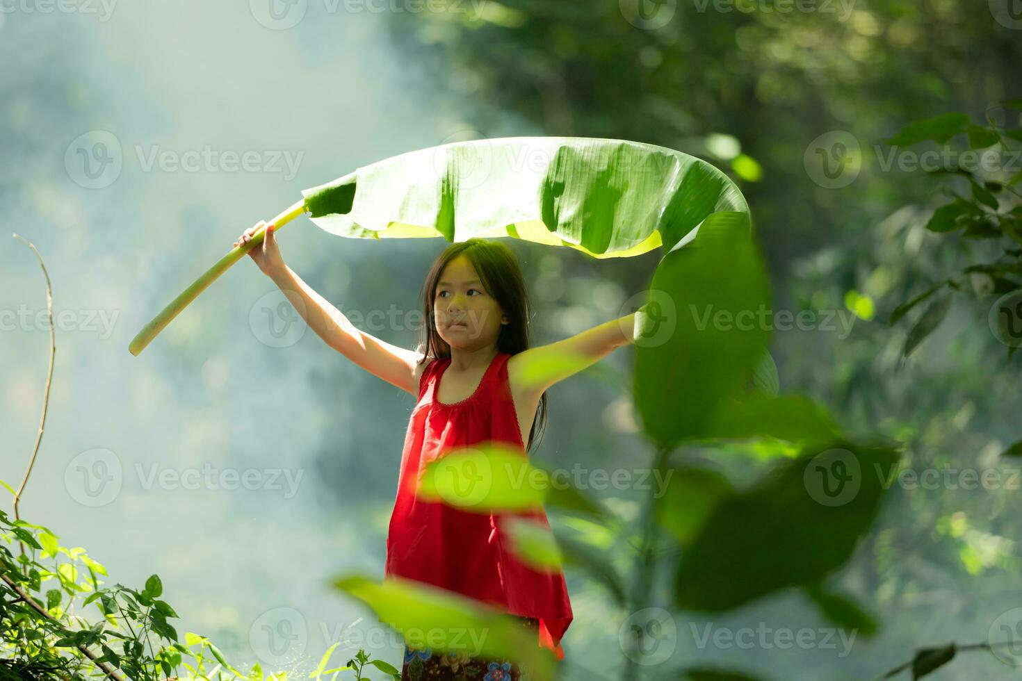 Little asian girl in red dress holding fishing equipment in the forest, Rural Thailand living life concept photo