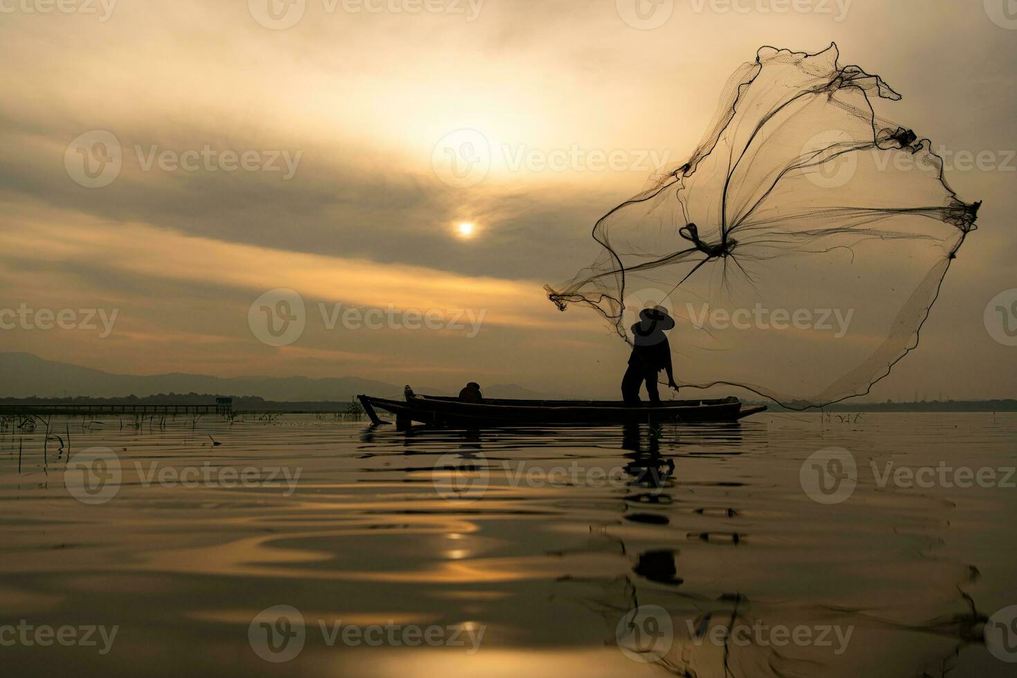 Silhouette of fisherman at sunrise, Standing aboard a rowing boat and casting a net to catch fish for food photo