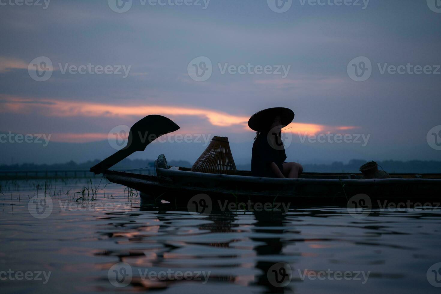 Silhouette of fisherman at sunrise, Standing aboard a rowing boat and casting a net to catch fish for food photo