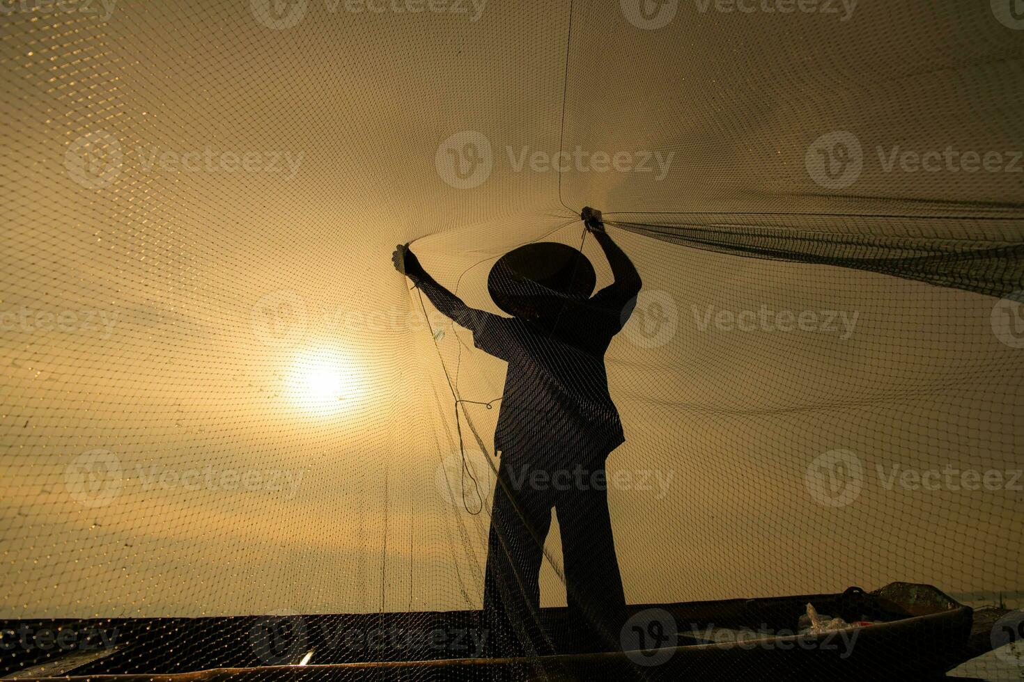 Silhouette of fisherman at sunrise, Standing aboard a rowing boat and casting a net to catch fish for food photo