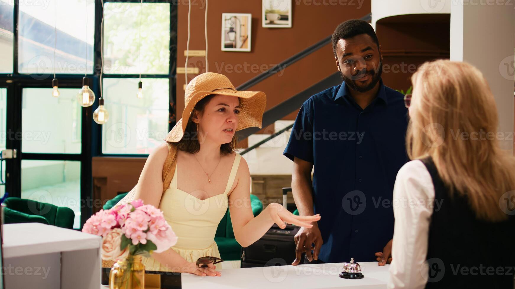 Hotel guests waiting to register at front desk, feeling excited about summer vacation at tropical luxury resort. Couple in lounge area before doing check in process and see room. Handheld shot. photo