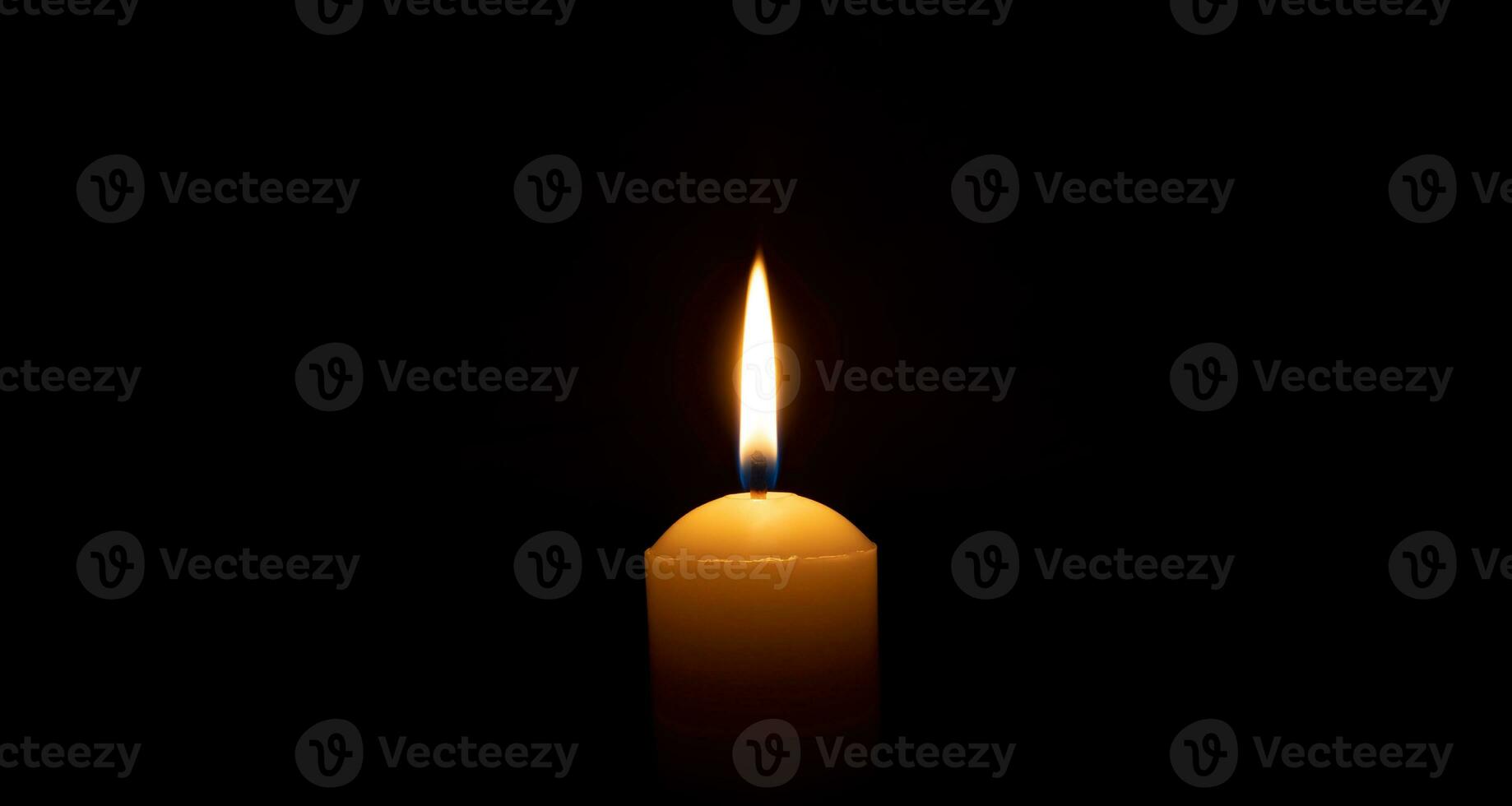 Single burning candle flame or light glowing on a big white candle on black or dark background on table in church for Christmas, funeral or memorial service with copy space. photo