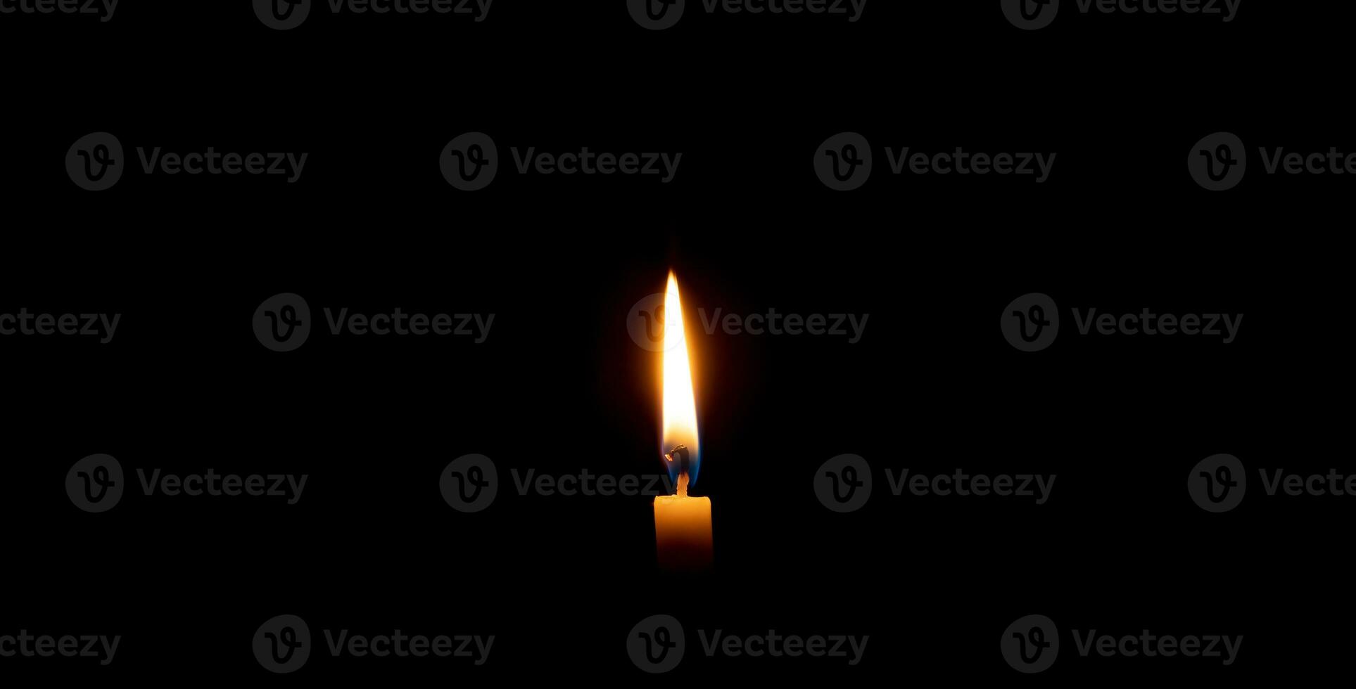 A single burning candle flame or light glowing on an orange candle on black or dark background on table in church for Christmas, funeral or memorial service with copy space photo