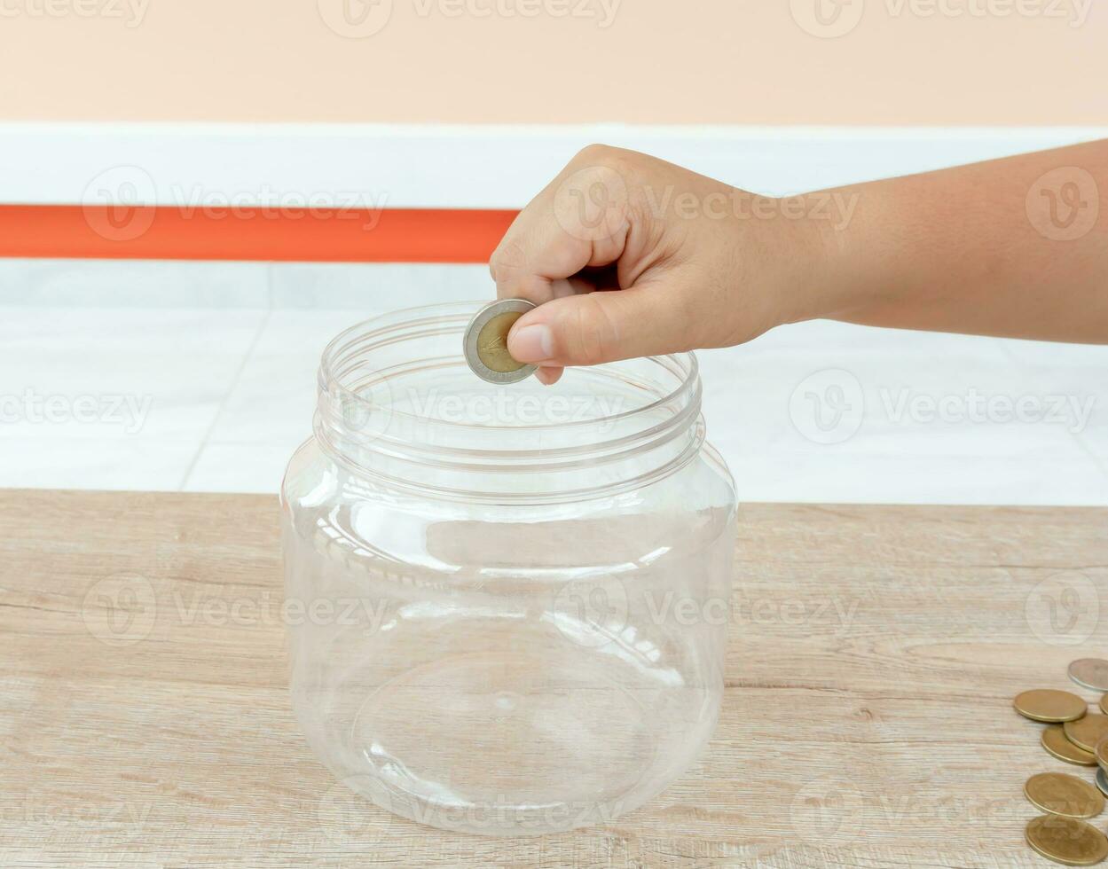 Child hand putting coin into plastic money bottle or piggy bank. Concept of saving money for the future or money growth photo