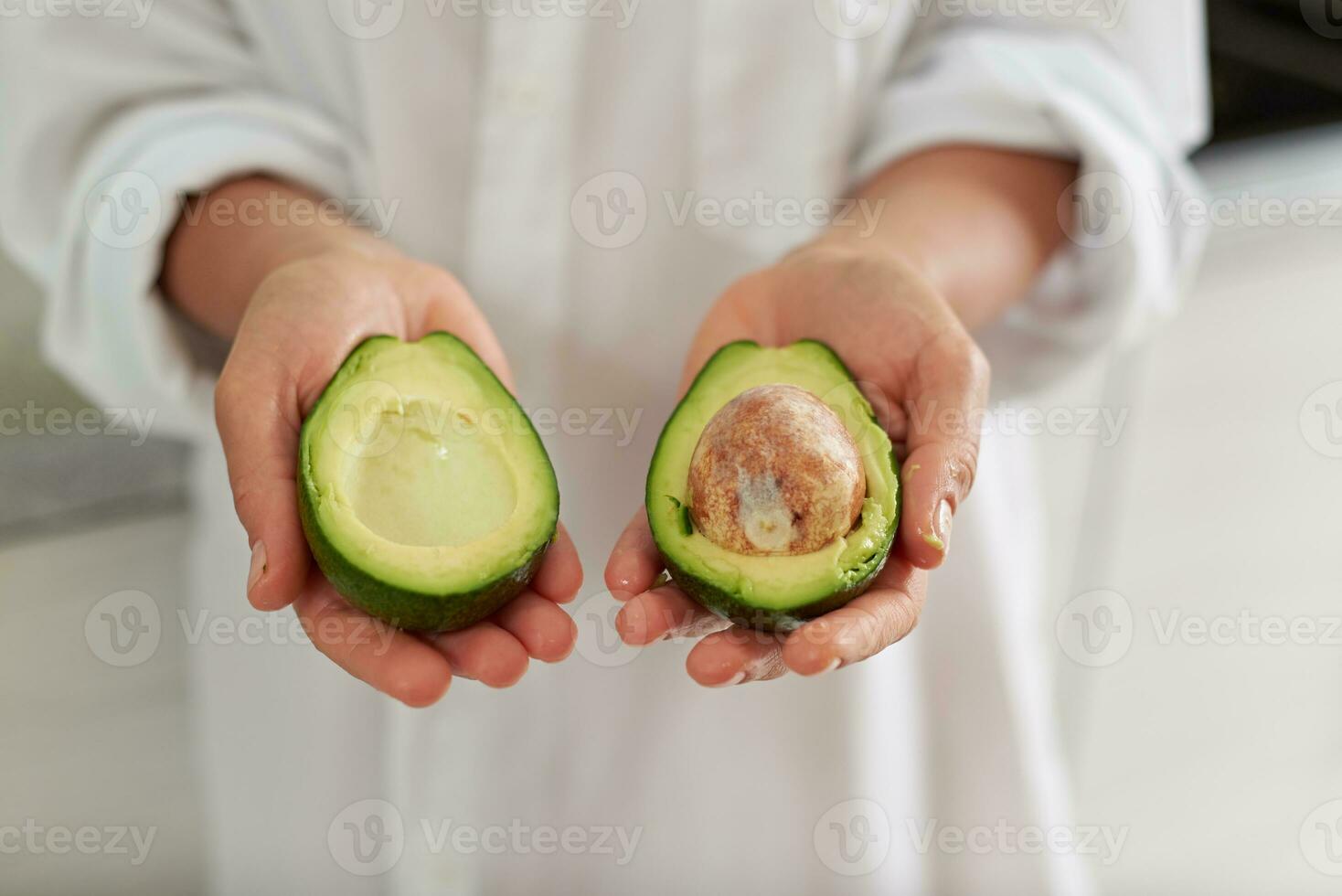 Closeup woman hands holding out at camera halves of ripe organic avocado fruit. Healthy eating, vegetarianism, dieting photo