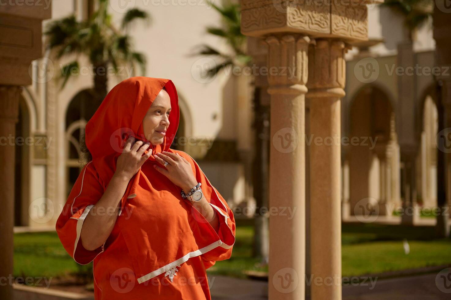 Lovely Muslim woman with head covered in hijab, looking into the distance, standing against Oriental building background photo