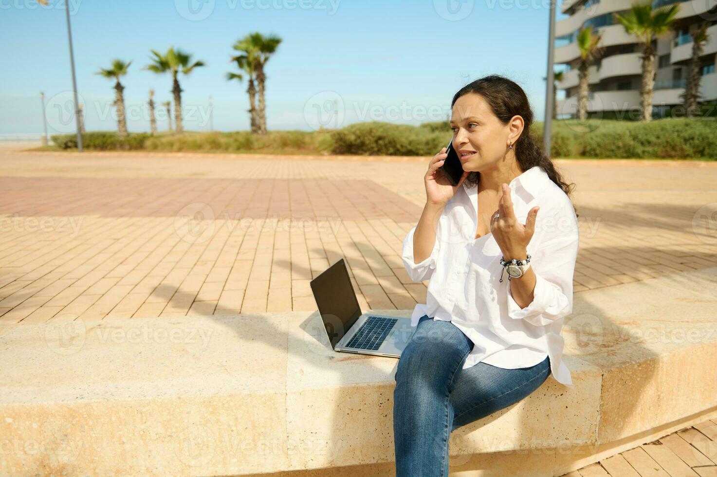 confidente joven mujer hablando móvil teléfono mientras trabajando en línea al aire libre, negociando nuevo puesta en marcha con negocio socios foto