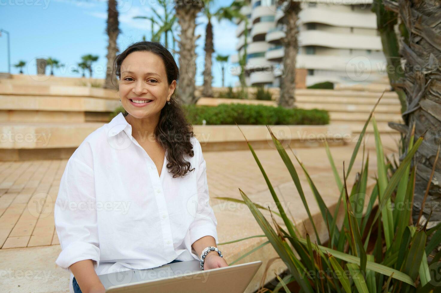 Confident young adult female entrepreneur remotely works on laptop, smiling looking at camera, planning business startup photo