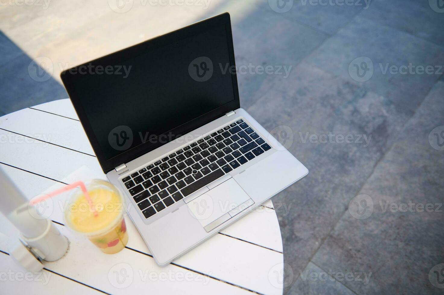 Still life with a laptop with black blank mockup screen with free advertising space for text and glass of orange juice photo