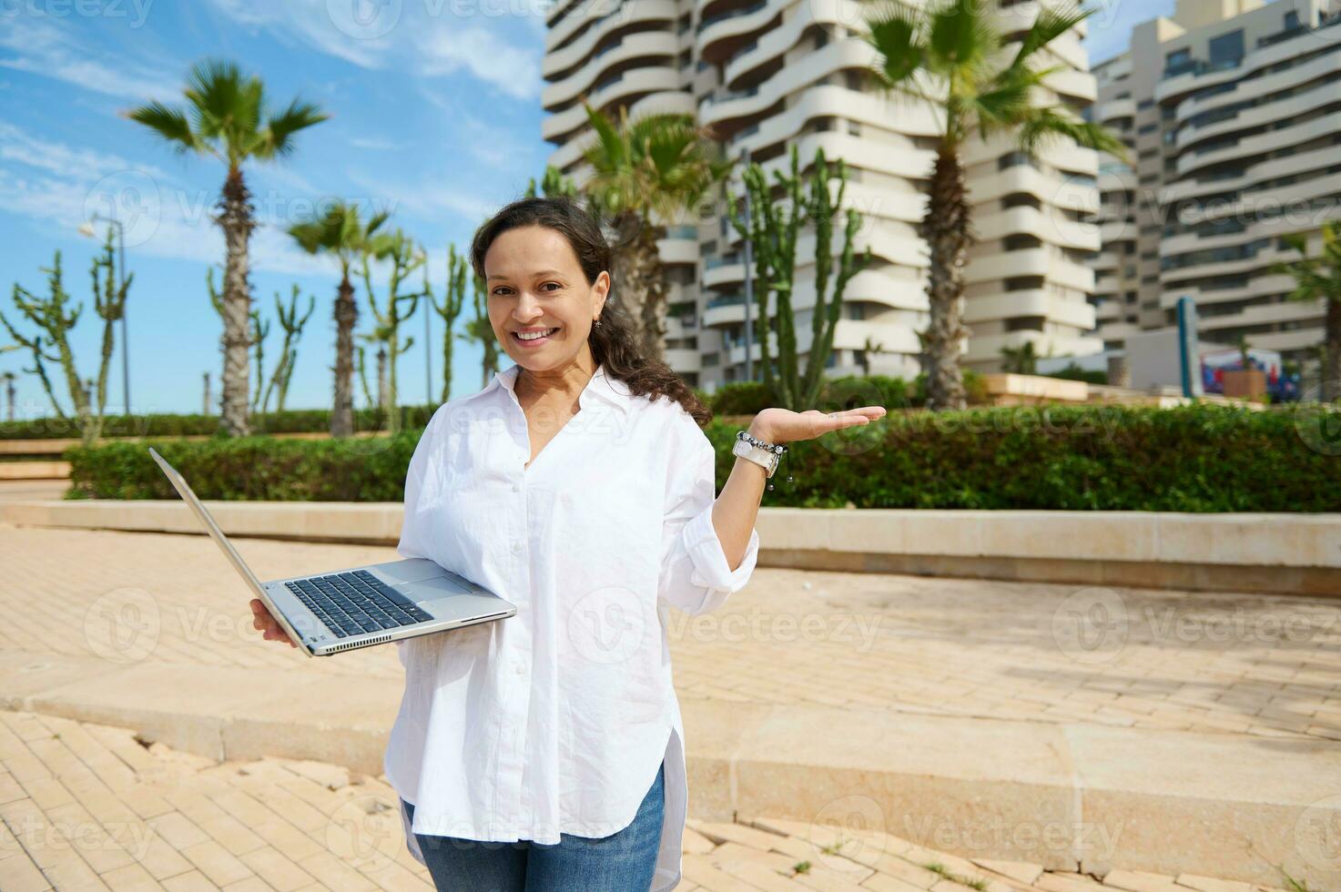 Confident young woman real estate holding laptop and copy space on her hand palm up. People. Business. Sales management photo