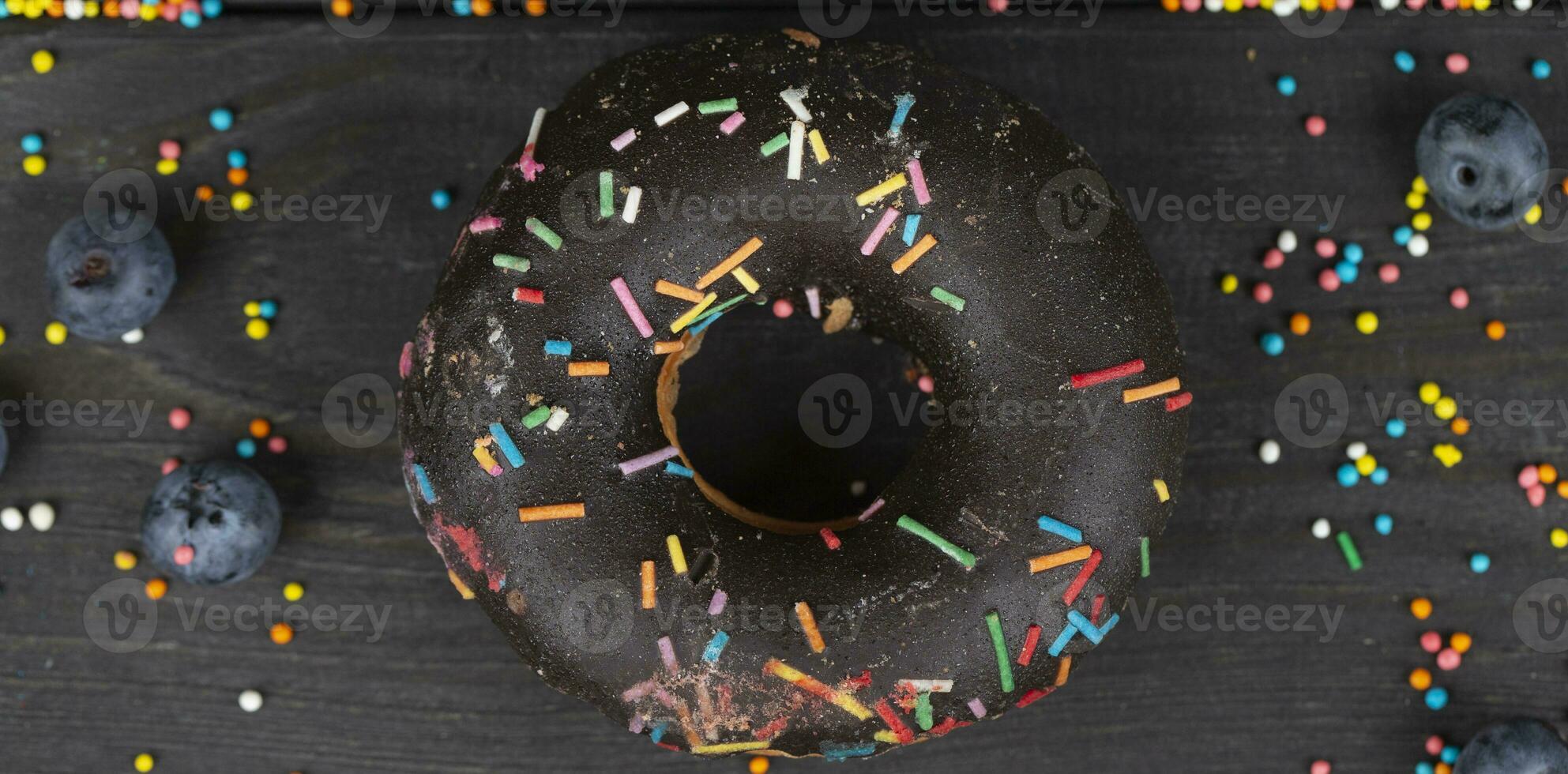 Beautiful sweet food. Colorful chocolate donut with colored sprinkles on a wooden background. photo