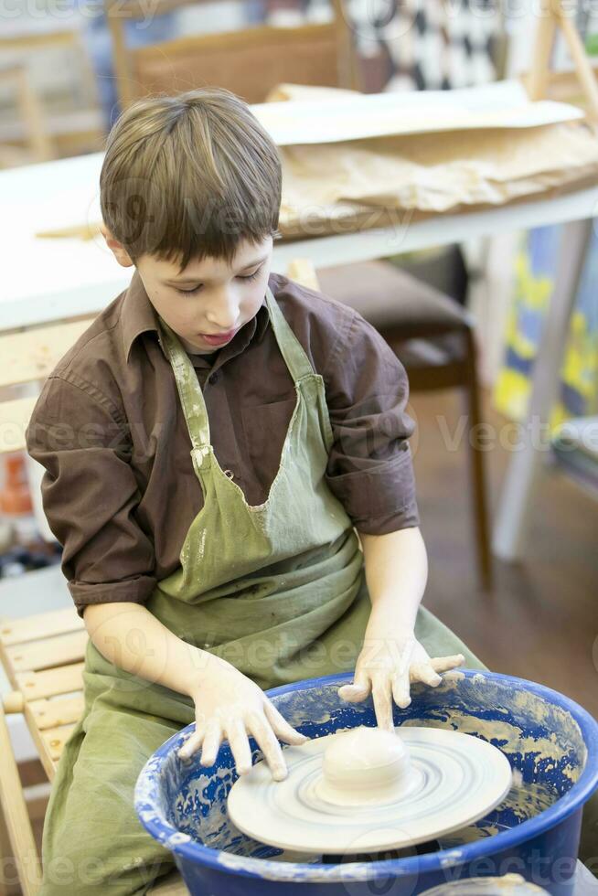 A little boy makes a clay product at a potter's wheel. photo