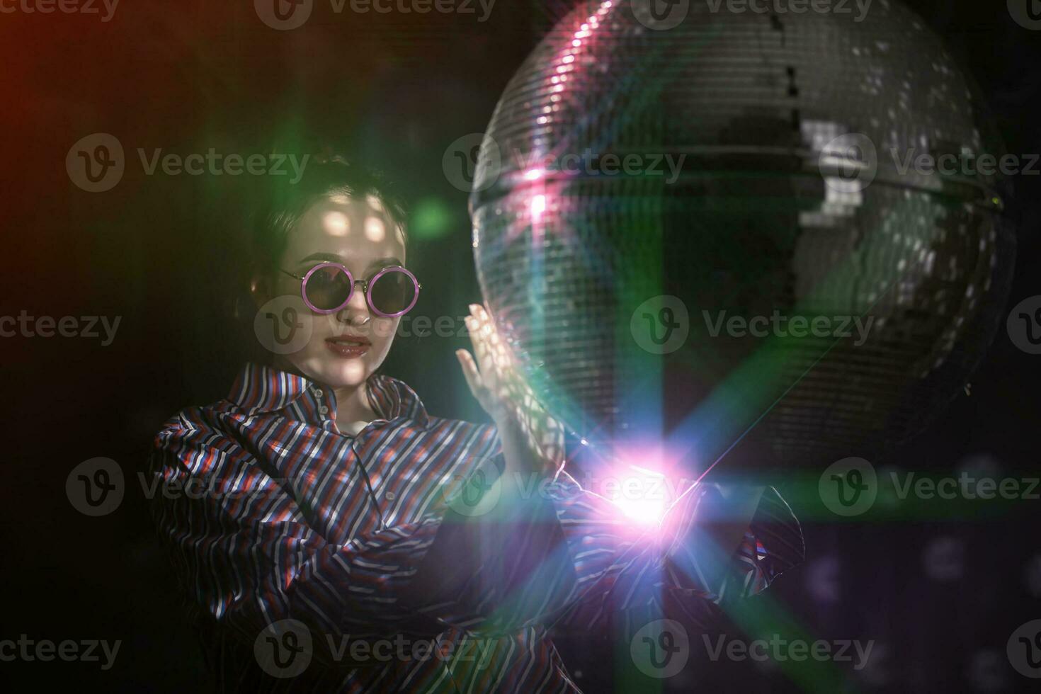 A beautiful girl in stylish glasses is spinning a sparkling disco ball. photo