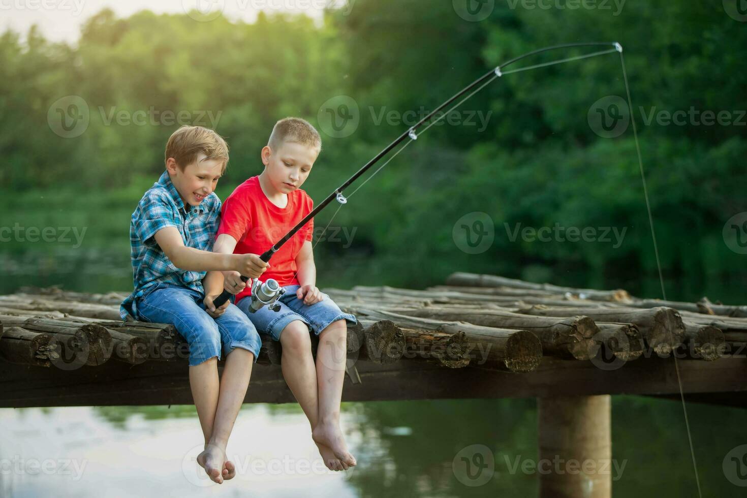 Two boy friends are sitting on a wooden bridge and fishing. Children on a fishing trip. photo