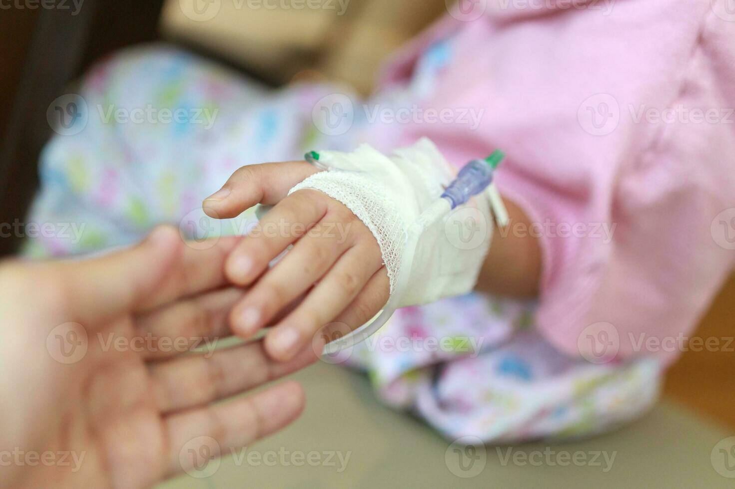 Mother holding child hand with saline IV solution in hospital photo