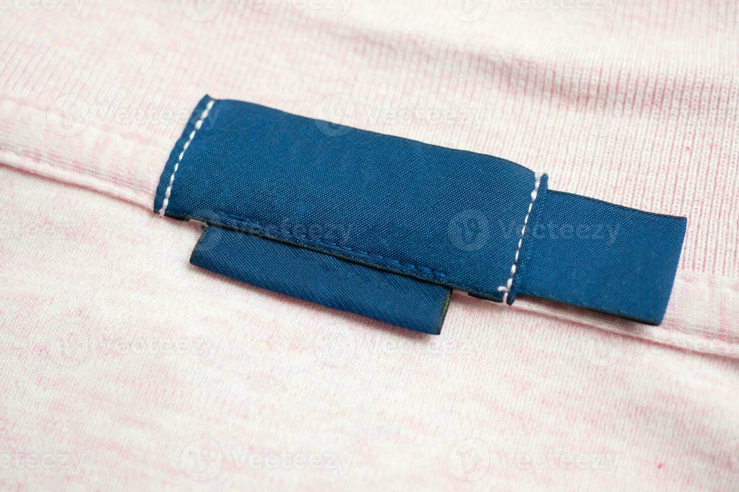 Blank blue laundry care clothes label on pink shirt fabric texture background photo