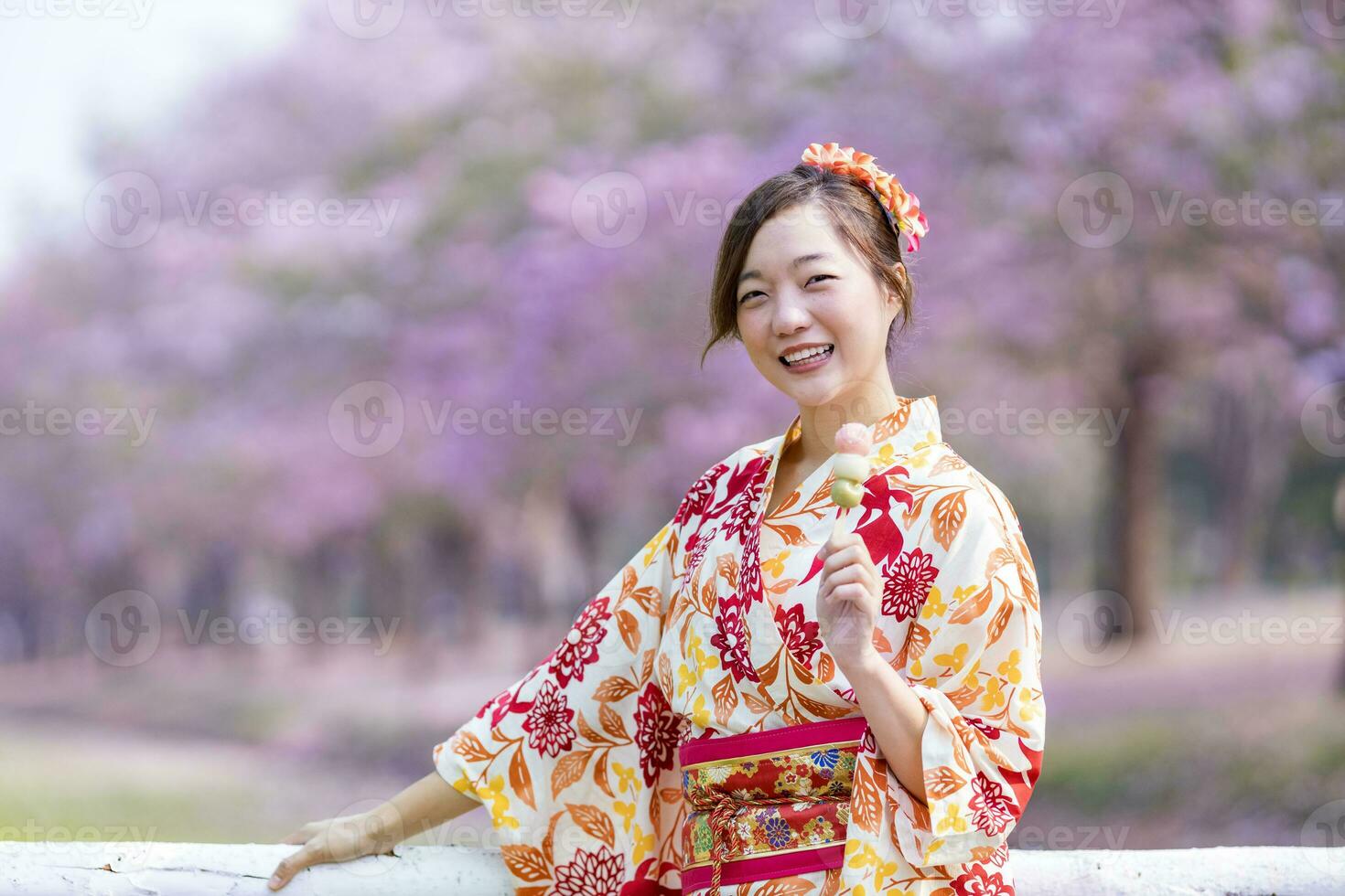 japonés mujer en tradicional kimono vestir participación dulce hanami dango postre mientras caminando en el parque a Cereza florecer árbol durante primavera sakura festival concepto foto