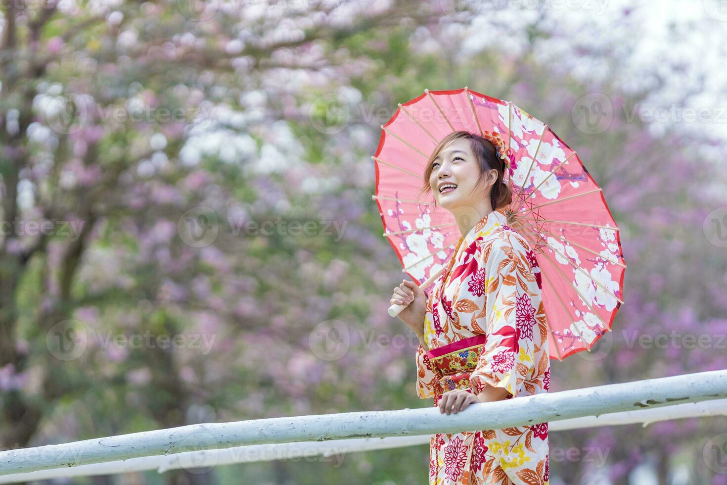 Japanese woman in traditional kimono dress holding umbrella and sweet hanami dango dessert while walking in the park at cherry blossom tree during the spring sakura festival photo